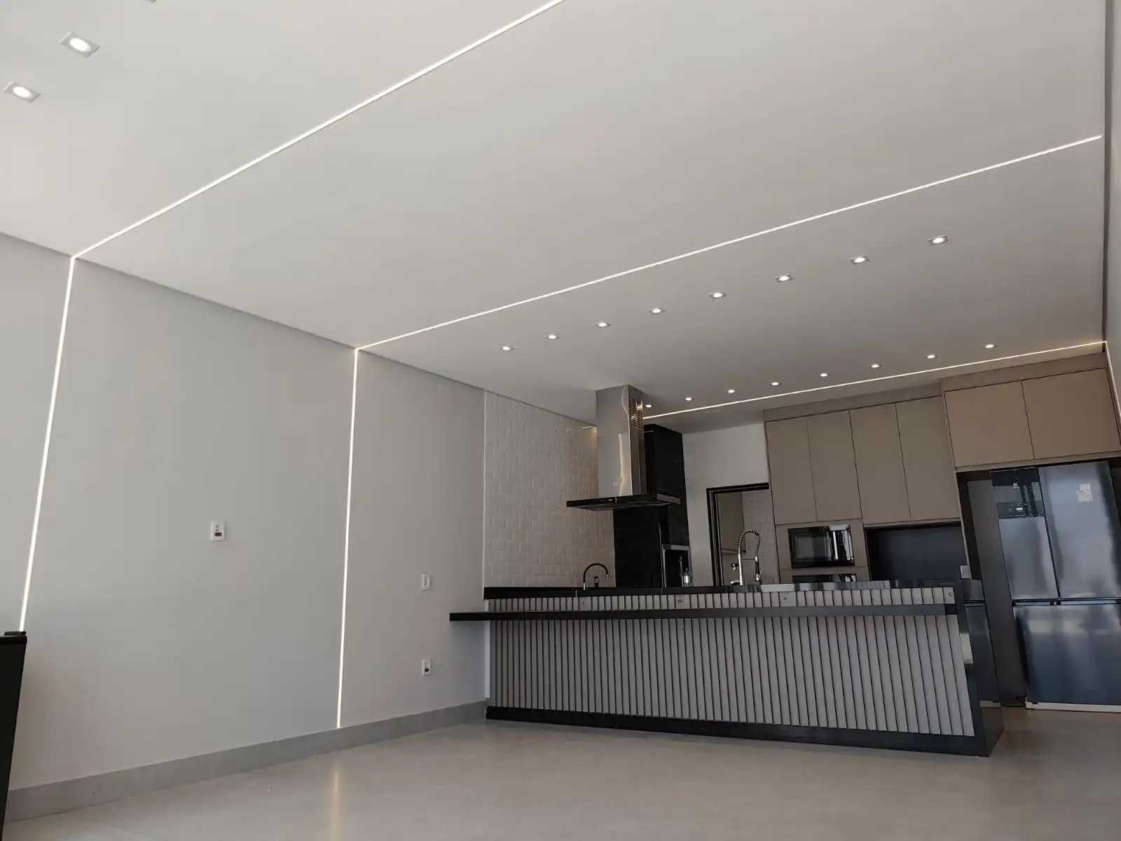 Cozinha valorizada pela nova iluminação LED — com perfis de luz embutidos que acompanham a arquitetura e spots estrategicamente posicionados para destacar a bancada, a marcenaria e os detalhes do ambiente.